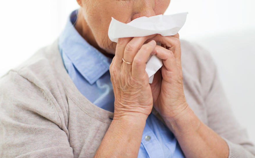 An elderly woman blowing her nose.